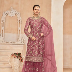 Op de afbeelding: Een roze geborduurde jurk met een bijpassende dupatta. De jurk heeft een top met lange mouwen en een uitlopende onderkant. De dupatta is doorschijnend en heeft een bloemenmotief. De jurk is versierd met gouden borduurwerk. D.NO: 7701