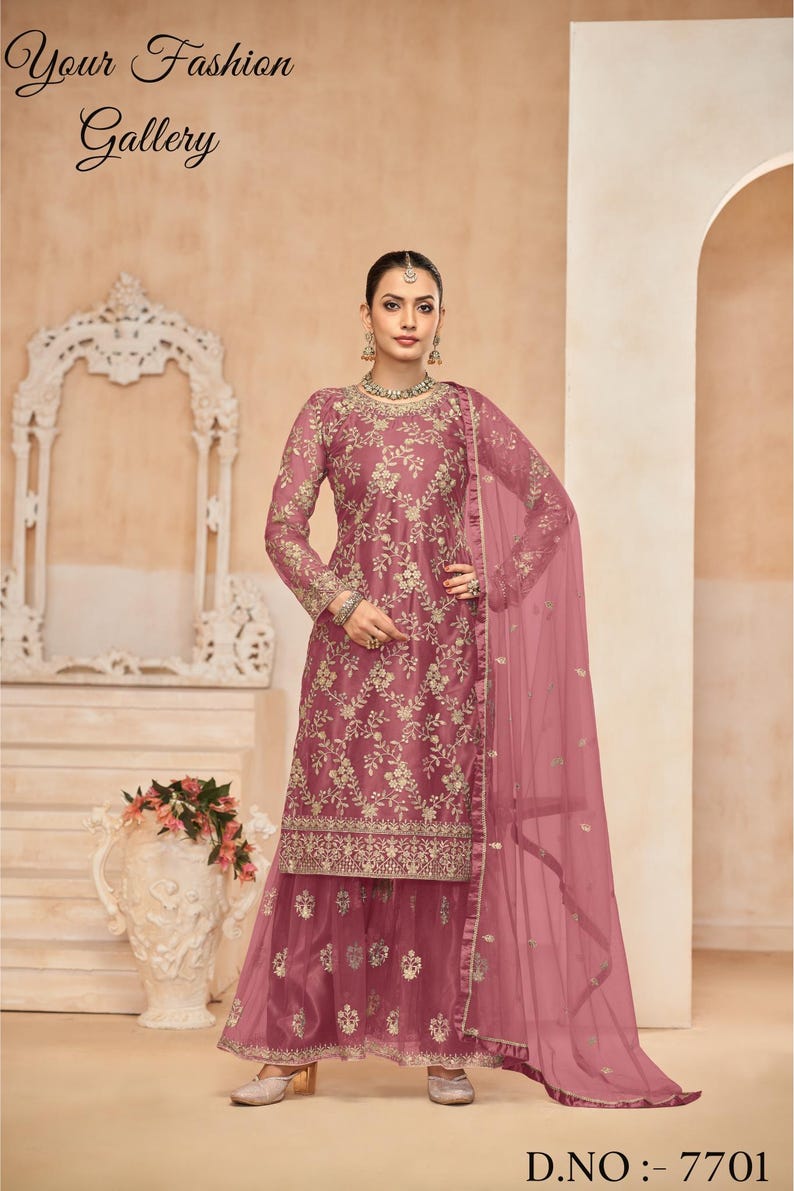 Op de afbeelding: Een roze geborduurde jurk met een bijpassende dupatta. De jurk heeft een top met lange mouwen en een uitlopende onderkant. De dupatta is doorschijnend en heeft een bloemenmotief. De jurk is versierd met gouden borduurwerk. D.NO: 7701