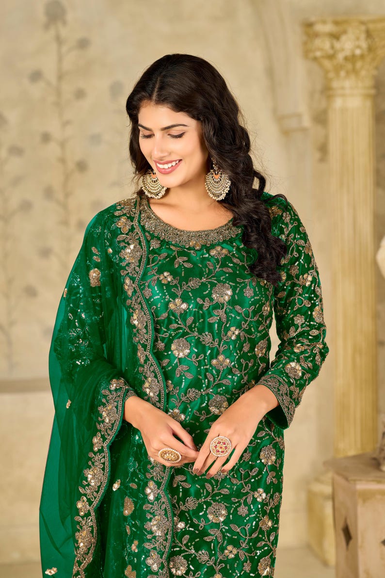 Pu&ograve; includere: Una tunica verde smeraldo a maniche lunghe con intricati ricami floreali dorati e decorazioni di paillettes sul corpetto e sulle maniche, abbinata a una dupatta verde trasparente coordinata con un bordo ricamato decorativo.