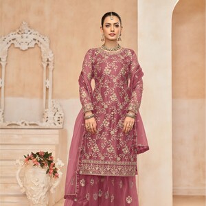 Op de afbeelding: Een roze geborduurde jurk met een bijpassende dupatta en palazzo broek. De jurk heeft een bloemenmotief en gouden borduurwerk. De dupatta is doorschijnend en heeft een gouden rand. De palazzo broek is wijd en heeft een gouden rand. D.NO: 7701