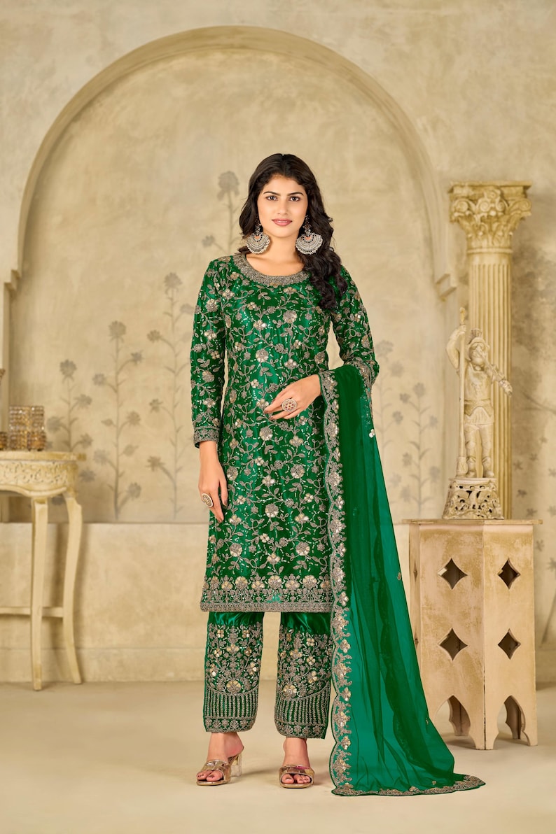 Pu&ograve; includere: Un completo composto da una tunica a maniche lunghe e pantaloni corti color verde smeraldo, caratterizzato da intricati ricami floreali argentati, paillettes e perline. L'insieme include una dupatta verde trasparente con bordo ricamato.