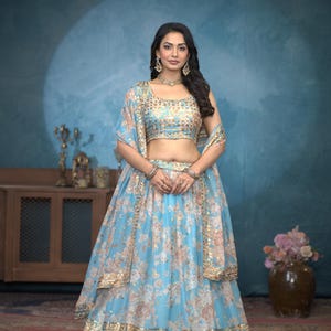 May include: A woman wearing a light blue and gold embroidered lehenga with a floral print. The lehenga has a matching embroidered choli and a sheer dupatta.