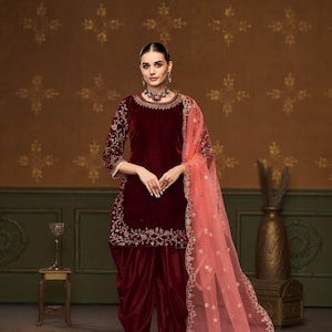 Puede incluir: Un salwar kameez de terciopelo granate con bordados dorados. El kameez tiene un escote redondo y mangas tres cuartos. El salwar es un pantal&oacute;n holgado con pliegues en la cintura. El atuendo se combina con un dupatta de red melocot&oacute;n con bordados dorados.