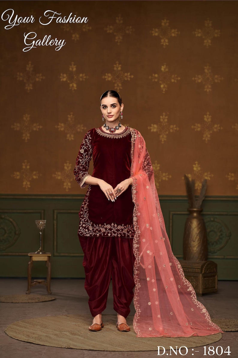 Puede incluir: Un salwar kameez de terciopelo granate con bordados dorados. El kameez tiene un escote redondo y mangas tres cuartos. El salwar es un pantal&oacute;n holgado con pliegues en la cintura. El atuendo se combina con un dupatta de red melocot&oacute;n con bordados dorados.