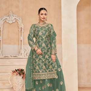 Op de afbeelding: Een groene geborduurde jurk met een bijpassende dupatta en palazzo broek. De jurk heeft een ronde halslijn en lange mouwen. De stof is doorschijnend en heeft een bloemenpatroon. De jurk is versierd met gouden borduurwerk. De outfit is perfect voor een speciale gelegenheid.