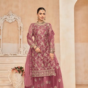 Op de afbeelding: Een roze geborduurde jurk met een bijpassende dupatta en palazzo broek. De jurk heeft een bloemenmotief en gouden borduurwerk. De outfit is perfect voor een speciale gelegenheid.