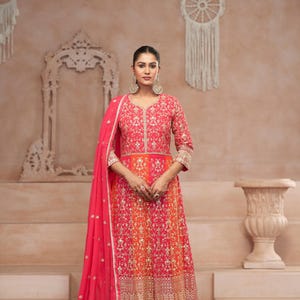 Może przedstawiać: Różowa i pomarańczowa haftowana sukienka z dopasowanym różowym dupattą. Sukienka ma dekolt w kształcie litery V i trzy czwarte rękawa. Dupatta jest zarzucony na ramiona kobiety. D.NO: 5417