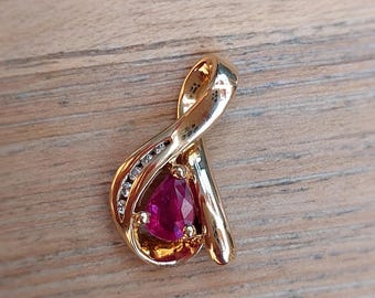 Op de afbeelding: Een gouden hanger met een rode edelsteen en kleine heldere stenen in een gedraaid ontwerp.