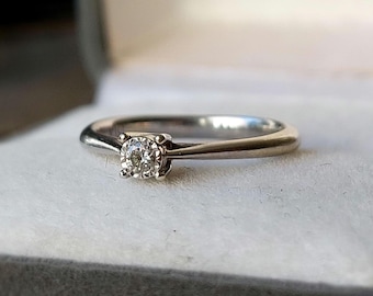 Puede incluir: Un anillo de banda de plata simple con un solo diamante redondo pequeño.