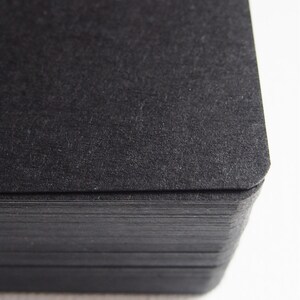 May include: A close-up of a stack of black card stock paper. The paper has a textured surface and is slightly rough to the touch.