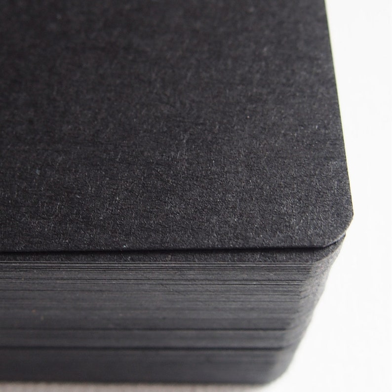 May include: A close-up of a stack of black card stock paper. The paper has a textured surface and is slightly rough to the touch.