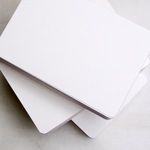 May include: A stack of blank, white rectangular cards with rounded corners. The cards are stacked neatly, with the top card slightly offset, revealing the edges of the cards below. The cards have a smooth, clean surface, suitable for writing or printing.