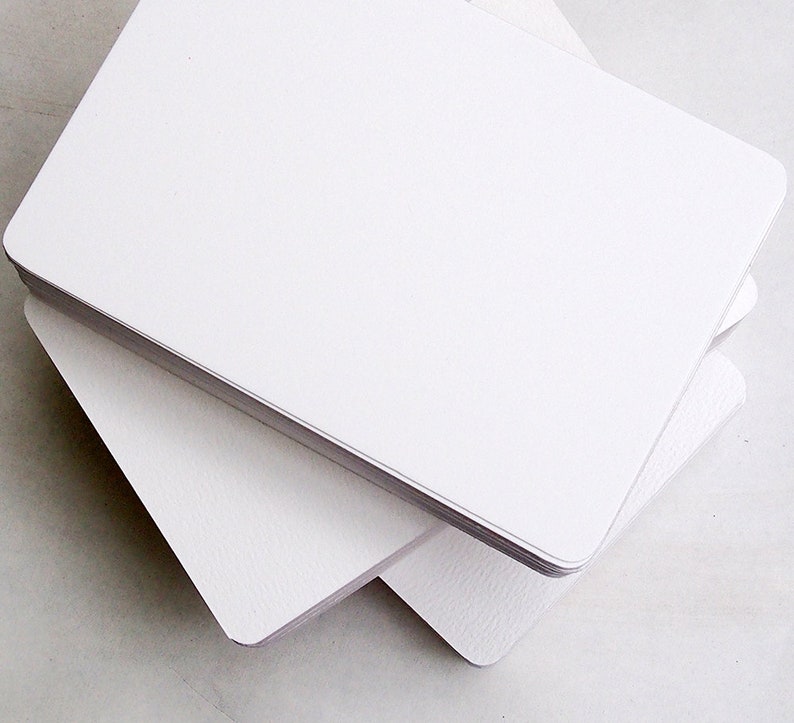 May include: A stack of blank, white rectangular cards with rounded corners. The cards are stacked neatly, with the top card slightly offset, revealing the edges of the cards below. The cards have a smooth, clean surface, suitable for writing or printing.