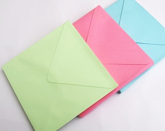 May include: Three envelopes stacked on top of each other. The top envelope is light blue, the middle envelope is pink, and the bottom envelope is light green.