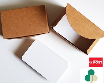 May include: Three brown cardboard boxes with a white card inside. The boxes are on a white surface. The card is blank and has rounded corners. The boxes are for storing cards or other small items.