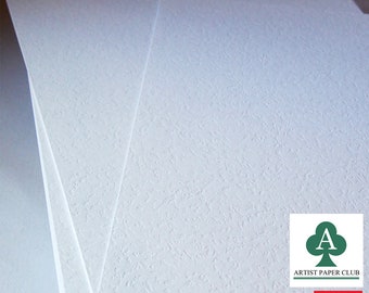 May include: A stack of white textured paper sheets. The paper has a subtle, rough texture. The sheets are stacked on top of each other, with the top sheet slightly angled. The image also includes a logo for "Artist Paper Club" and a logo for "Australia Post".