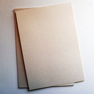 May include: Two sheets of beige textured paper stacked on top of each other. The paper has a speckled appearance.