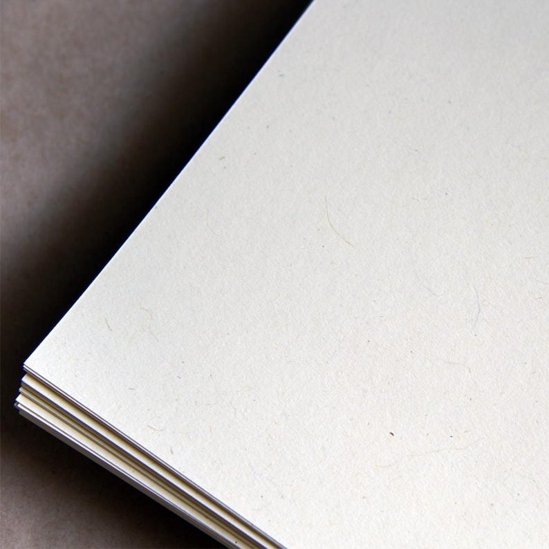 Op de afbeelding: Een stapel cr&egrave;mekleurige vellen papier met een licht gestructureerd oppervlak.