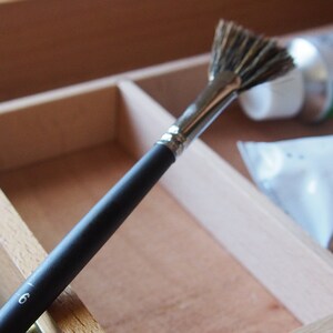 May include: A black handled fan brush with silver ferrule and a number 6 printed on the handle. The brush is in a wooden box with a white tube and a clear plastic bag.