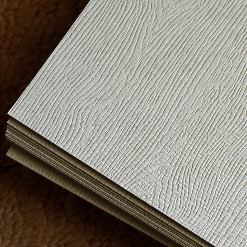 May include: Close-up of a stack of white woodgrain-textured panels. The panels have a subtle embossed pattern that resembles wood grain.