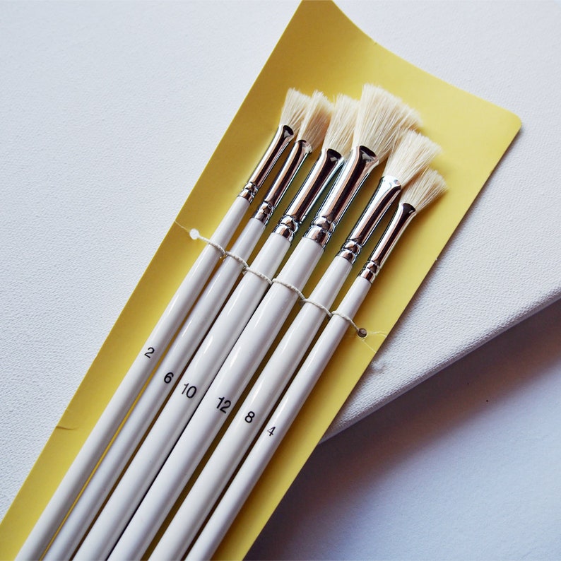May include: Set of six white paint brushes with yellow handles. The brushes are labeled with numbers 2, 6, 10, 12, 8, and 4.