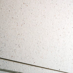 May include: Close-up of a stack of white textured paper with flecks of brown throughout.