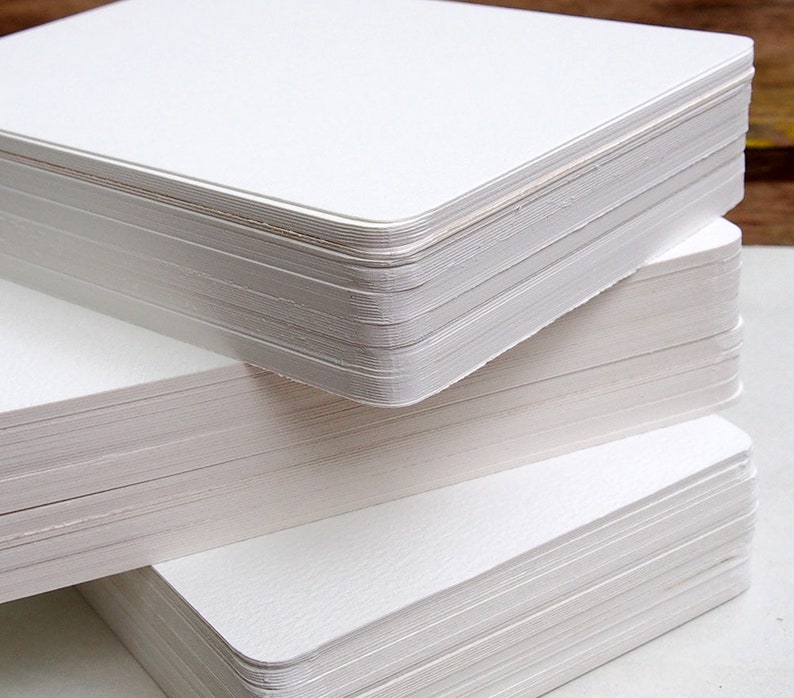May include: Close-up of three stacks of white, rectangular cards with rounded corners. The cards are neatly stacked, revealing the edges of each individual card. The paper appears to have a slightly textured surface, and the overall presentation is clean and minimalist.