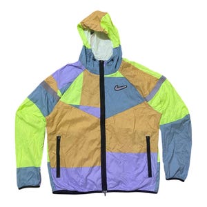 May include: A multi-colored Nike windbreaker jacket with a hood. The jacket features a patchwork design in shades of yellow, blue, purple, and tan. It has a black zipper and the Nike swoosh logo on the chest.