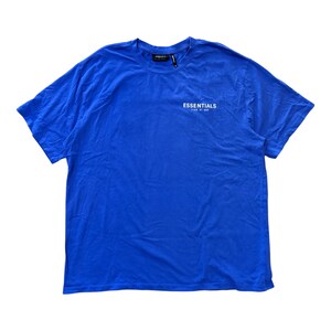 May include: A vibrant blue t-shirt with the word "ESSENTIALS" printed in white on the front. The shirt is a solid color and appears to be made of a soft material. The text "FEAR OF GOD" is printed below "ESSENTIALS".