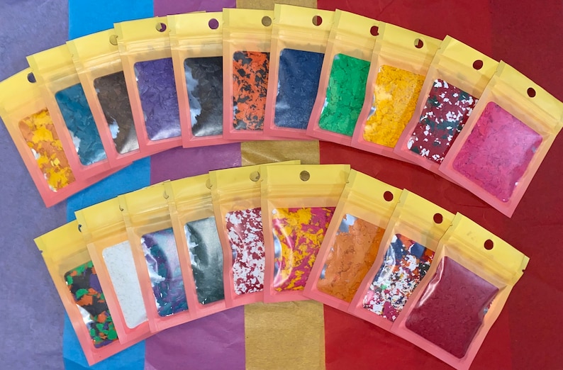 K&ouml;nnte beinhalten: Eine Sammlung kleiner, klarer Plastikt&uuml;ten, gef&uuml;llt mit bunten, unregelm&auml;&szlig;ig geformten Flocken. Die Flocken variieren in der Farbe, darunter Gelb, Blau, Orange und Lila. Jede T&uuml;te ist versiegelt und hat einen gelben Deckel.