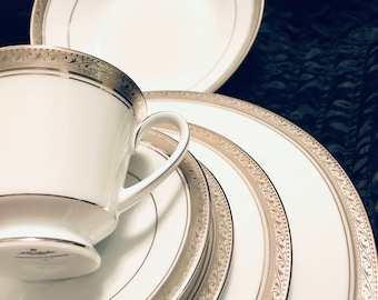 May include: A set of white porcelain dinnerware with gold trim and a delicate floral pattern. The set includes a cup, saucer, and three plates.