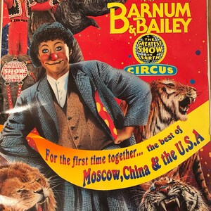 May include: A vintage circus poster featuring a clown with a red nose and a blue suit. The poster advertises Ringling Bros. and Barnum & Bailey Circus, with the text "The Greatest Show on Earth". The poster also features a tiger, a lion, and an elephant.