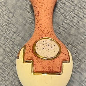 May include: A decorative vase with a speckled peach-colored upper section and a cream-colored base. The vase features a circular design with a speckled center and gold trim. The vase is approximately 8 inches tall.