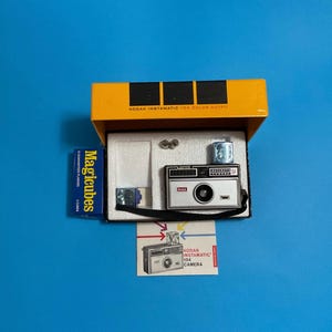 May include: A vintage Kodak Instamatic 104 Color Outfit camera kit. The kit includes a silver and black camera, flash, and a box of Magicubes. The camera is in an open yellow box with the text "KODAK INSTAMATIC 104 COLOR OUTFIT".