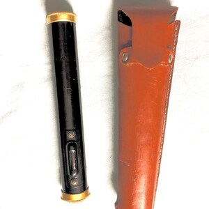 May include: A vintage black and gold surveyor's level with a brown leather carrying case. The level has a bubble indicator and gold-colored accents on both ends. The leather case is a rich brown color and has a flap closure.