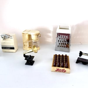 May include: A collection of miniature vintage items, including a black iron, a can opener, a coffee maker, a gramophone, a grater, a Pepsi-Cola crate, and a sewing machine. The items are arranged on a white surface.