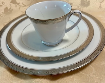 May include: A white porcelain teacup and saucer set with a silver trim and floral design.