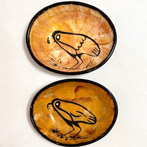 May include: Two oval-shaped ceramic bowls with a hand-painted design. The bowls have a warm, orange-brown interior with a black rim. Each bowl features a black bird illustration. The bowls are likely for serving food or as decorative items.