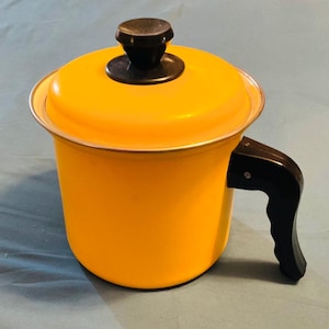 May include: A vintage yellow enamelware pot with a lid and a black handle. The pot has a silver rim and a black knob on the lid. The pot is likely used for cooking or serving.