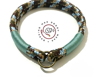 May include: A circular pet collar made of braided rope in shades of brown, tan, and light blue. The collar features two sections wrapped in sage green cord and a central bronze-toned metal ring. The logo BARKING MAD DOGGY WEAR is visible.