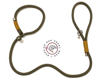 May include: An olive green rope dog leash featuring mustard yellow thread accents, silver metal hardware, and a circular logo in the center that reads BARKING MAD DOGGY WEAR with a stylized dog icon. The leash has two loops and a metal ring.