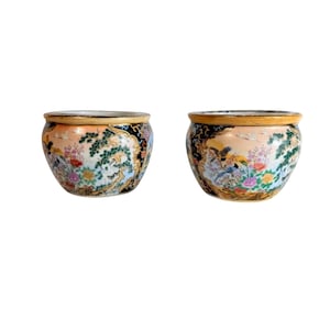 May include: Two matching ceramic bowls with a wide, rounded shape. The bowls feature a peach-colored background with a detailed painted scene of birds, flowers, and trees. The rims are trimmed with a gold band and black accents.
