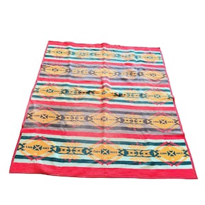 May include: A rectangular blanket with a Southwestern design. The blanket features horizontal stripes in red, gray, teal, and yellow. The design includes geometric patterns and diamond shapes. The blanket is made of a soft, woven material.