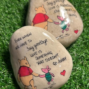 May include: Two painted stones featuring Winnie the Pooh and Piglet. The stones display the quote "Even when we have to say goodbye, love is something that doesn't go away".