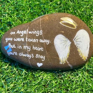 May include: A painted rock with the words "on Angel wings you were taken away. But in my heart you'll always stay" and a drawing of angel wings.