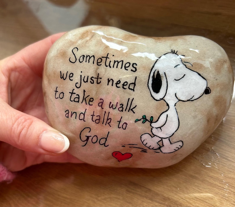 May include: A heart-shaped, painted stone with the text "Sometimes we just need to take a walk and talk to God." A cartoon Snoopy character is walking with a sprig of leaves. A red heart is painted below the text.