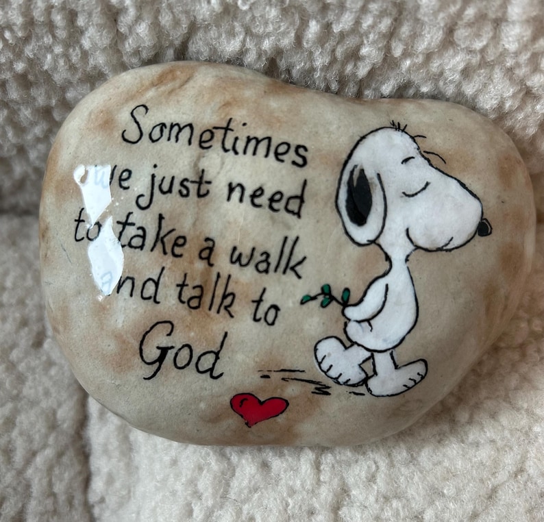 May include: A painted stone with the text "Sometimes we just need to take a walk and talk to God." A cartoon Snoopy character is walking with a sprig of leaves. A red heart is painted below the text.