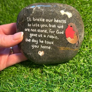 May include: A gray painted rock with a white painted message that reads "It broke our hearts to lose you, but we are not alone, for God gave us a robin, the day he took you home." A small white heart is painted on the rock. A painted robin with a red breast is on the rock.