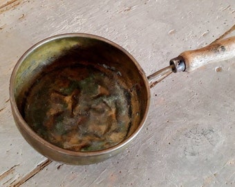 Old metal frying pan with a wooden handle. Vintage pot. Decoration for rustic kitchen. Old small pot. Old rusty metal.
