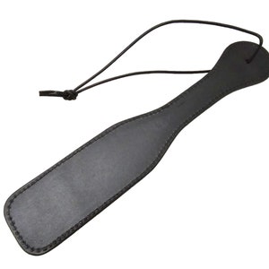 May include: A black leather paddle with a stitched edge and a loop handle.